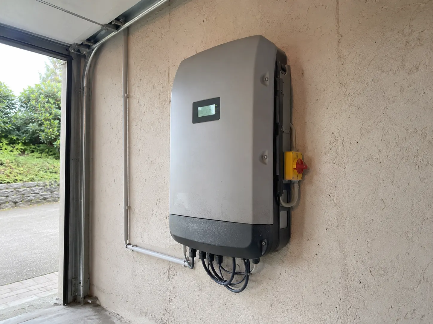 Fronius Symo Wechselrichter an einer rauh-verputzten Garagenwand mit DC-Trennschalter
